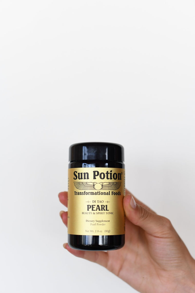 Hand holding a violet glass jar of Sun Potion Pearl